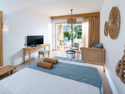 Camera d'hotel luminosa con letto matrimoniale, zona salotto, TV e accesso a balcone o terrazza.