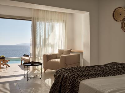 Camera d'hotel luminosa con vista mare e una poltrona accogliente vicino alla finestra.