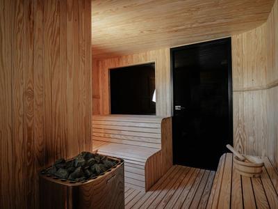 Sauna rivestita di legno con panca, riscaldatore con pietre e secchio di legno con mestolo.