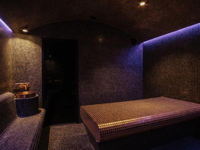 Accogliente stanza spa illuminata con due panche imbottite e luce viola soffusa.