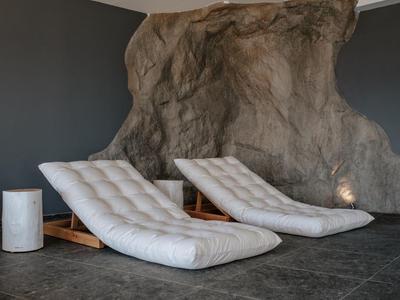 Due poltrone imbottite davanti a una parete rocciosa, accanto a un piccolo tavolo cilindrico su un pavimento scuro.