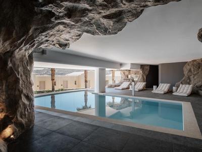 Piscina interna con parete rocciosa e lettini sotto un soffitto basso.
