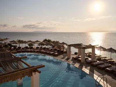 Area piscina resort con lettini e ombrelloni che si affaccia su un mare calmo al tramonto.