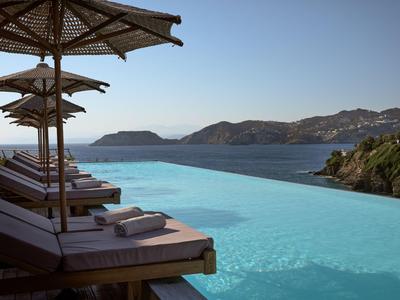 Piscina infinita con tumbonas y sombrillas con vistas al mar y colinas al fondo