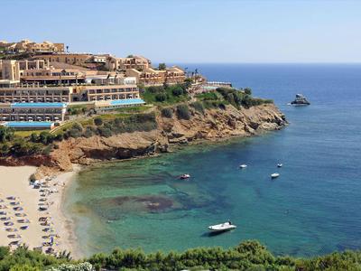 Vista di un resort su una costa rocciosa con acqua limpida e barche nel mare.