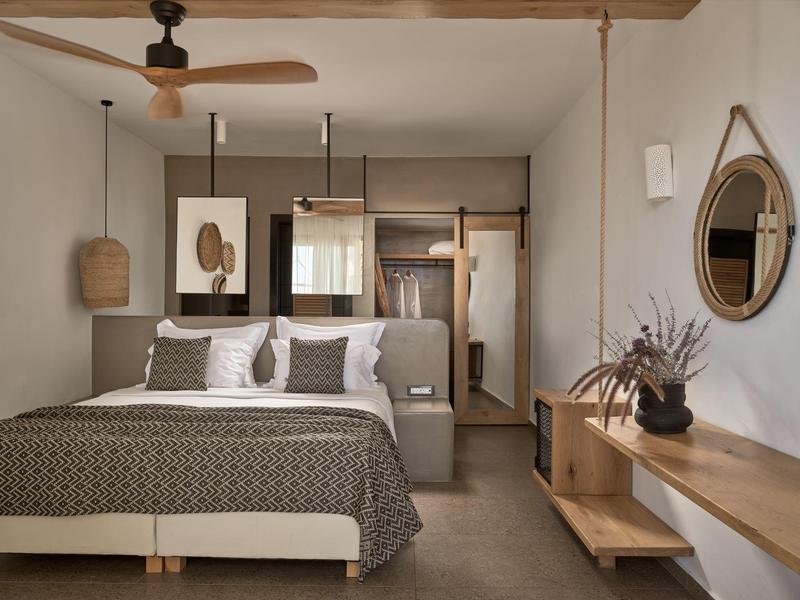 Camera d'hotel moderna con letto matrimoniale, ventilatore a soffitto, specchio e arredamento minimalista.