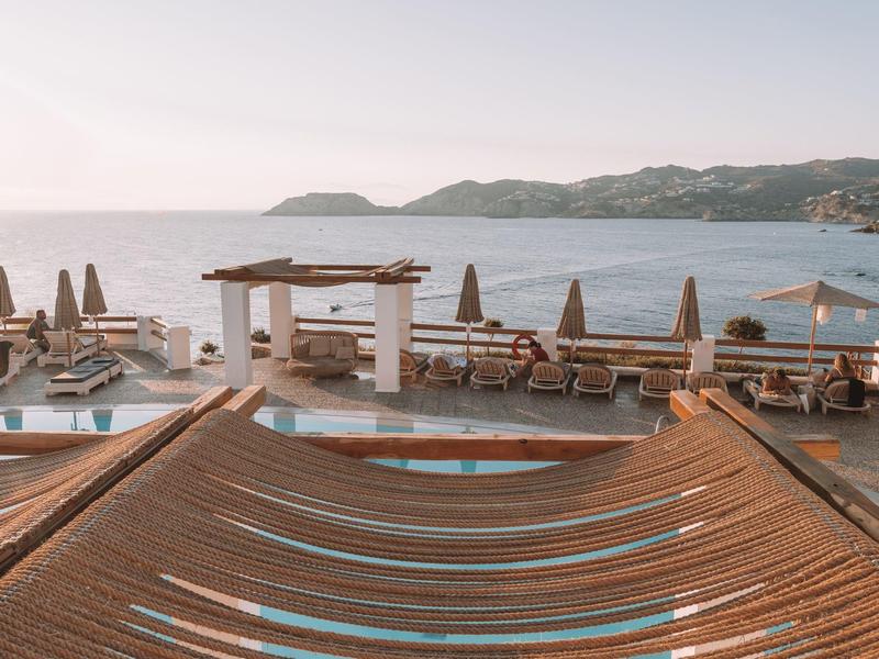 Lettini da spiaggia vicino a una piscina con vista mare e montagne sullo sfondo.
