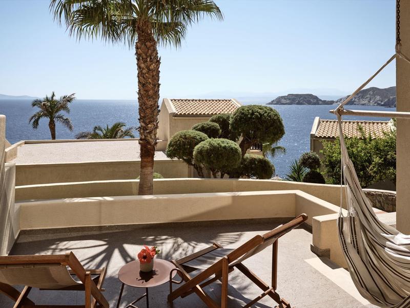 Terrazza con tavolo, sedie e amaca con vista sul mare e palme.