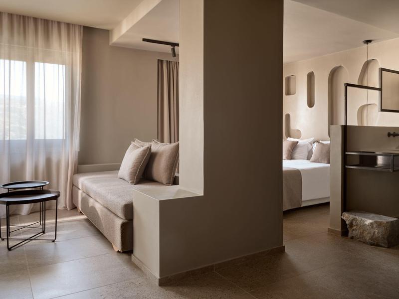 Camera d'hotel moderna con parete divisoria, divano, letto e arredamento minimalista.