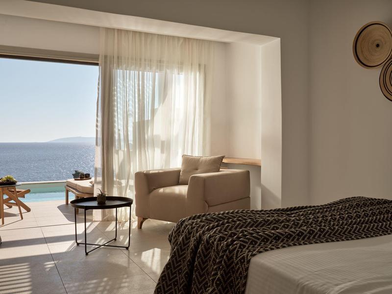 Camera d'hotel luminosa con vista mare e una poltrona accogliente vicino alla finestra.