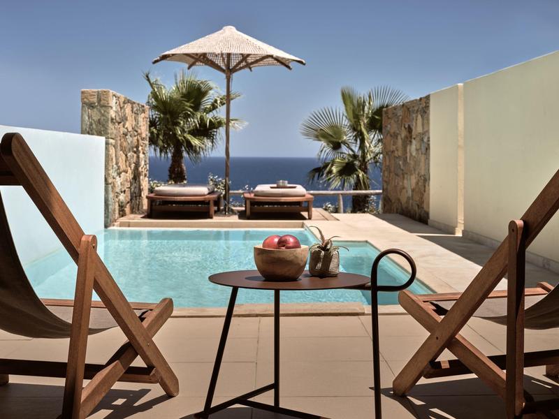 Zona piscina lussuosa con lettini, ombrellone e vista mare in una giornata soleggiata.