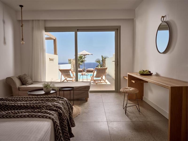 Camera d'hotel luminosa con letto, divano, scrivania e terrazza con vista mare.