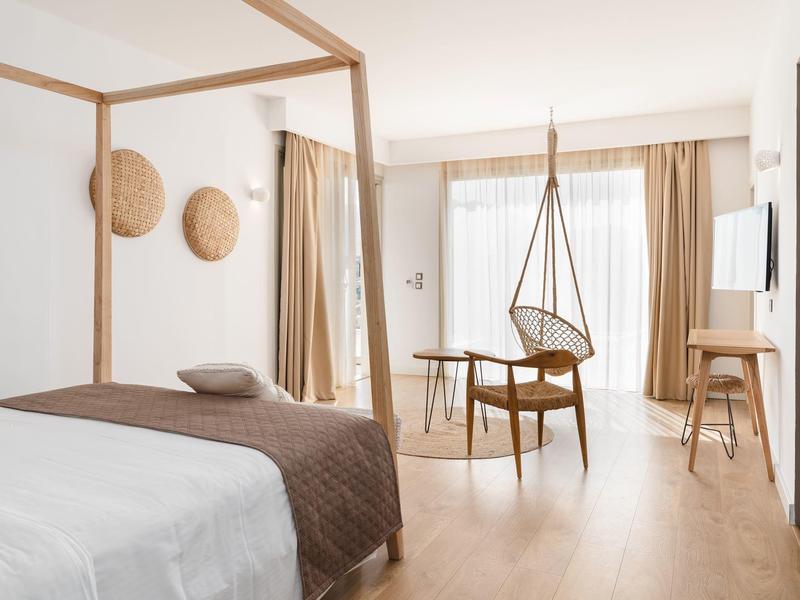 Camera d'hotel luminosa con pavimento in legno, letto a baldacchino e area salotto moderna.