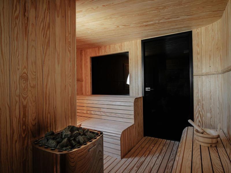 Sauna rivestita di legno con panca, riscaldatore con pietre e secchio di legno con mestolo.