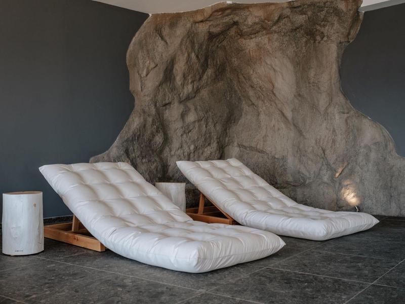 Due poltrone imbottite davanti a una parete rocciosa, accanto a un piccolo tavolo cilindrico su un pavimento scuro.