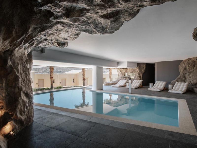 Piscina interna con parete rocciosa e lettini sotto un soffitto basso.