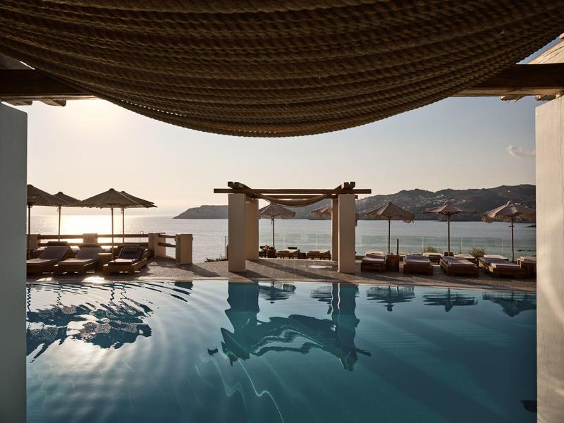 Piscina all'aperto con lettini e ombrelloni con vista sul mare calmo al tramonto.