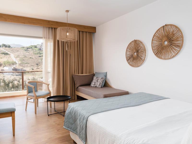 Camera d'hotel luminosa con letto matrimoniale, area salotto, pavimento in legno e vista sulle colline.