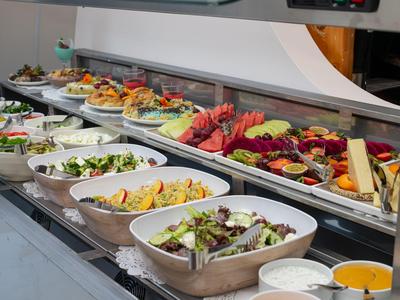 Bufé con varias ensaladas frescas y frutas en tazones blancos sobre una barra.