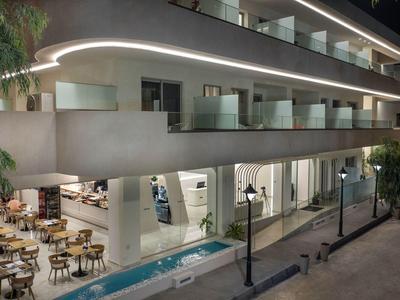 Moderna terraza de hotel con mesas, sillas y piscina iluminada junto a la fachada