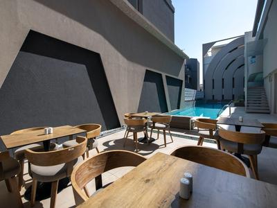 Restaurante exterior moderno con mesas y sillas de madera junto a una piscina bajo un cielo despejado.