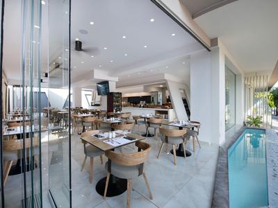 Restaurante moderno con sillas de madera y fachada de vidrio junto a una pequeña piscina