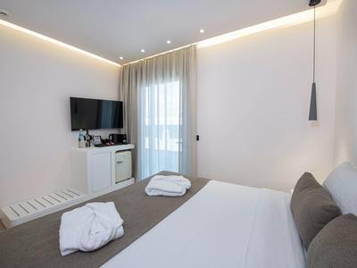 Modern hotel room with double bed, wall-mounted TV, and daylight through a window with curtain.