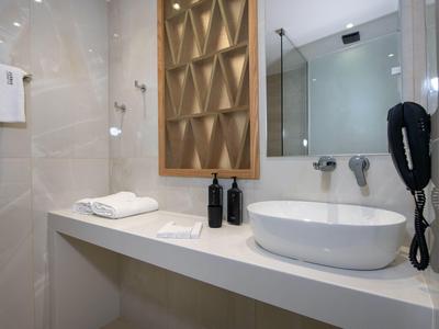 Modern hotel bathroom with sink, towels, and wall-mounted hairdryer.