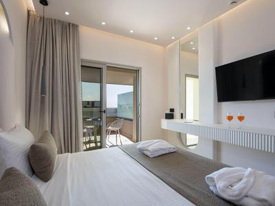 Habitación de hotel luminosa con cama doble, televisor y vista al mar a través de grandes puertas.