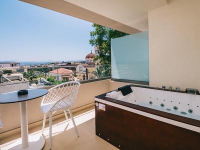 Balcony with hot tub, two chairs, and table overlooking city and sea under clear sky.