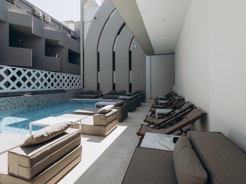 Modern outdoor pool area with loungers and sofas beside a hotel building.