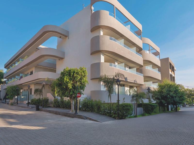 Modern multi-story hotel building with balconies under a clear sky.