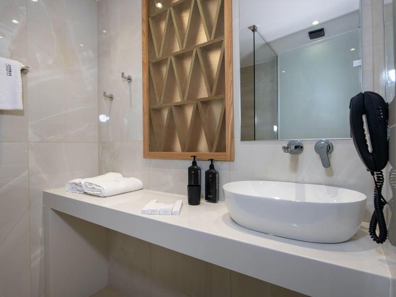 Modern hotel bathroom with sink, towels, and wall-mounted hairdryer.