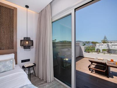 Moderner Hotelraum mit Einzelbett und Balkon mit Sitzbereich und Blick auf Gebäude.