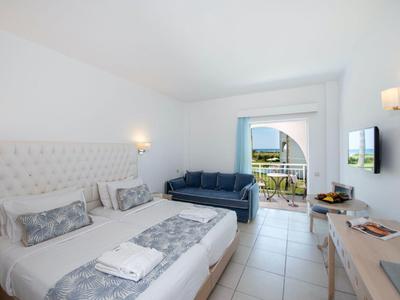 Helles Hotelzimmer mit Doppelbett, Sofa, Flachbildfernseher und Balkon mit Aussicht.