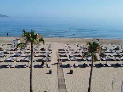 Strand mit Liegen, Sonnenschirmen und Palmen am ruhigen Meer bei klarem Himmel.