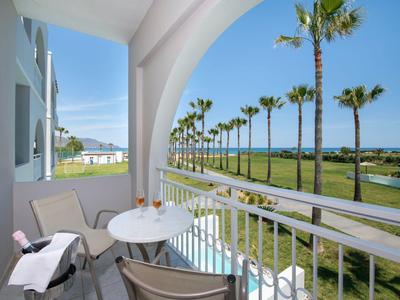 Balkon mit zwei Stühlen und Tisch, Blick auf Palmen, grünen Rasen und Meer im Hintergrund
