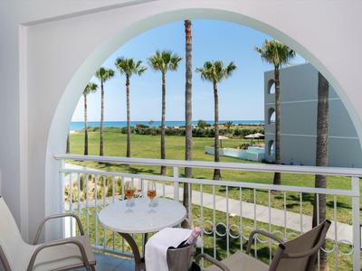 Balkon mit Tisch und Stühlen mit Blick auf palmenbestandenen Golfplatz und Meer.