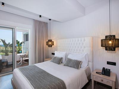 Hell eingerichtetes Hotelzimmer mit großem Bett und Zugang zu Balkon mit Pflanzen.