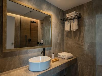 Modernes Badezimmer mit Wandspiegel, Waschbecken, Handtüchern und braunen Fliesen.