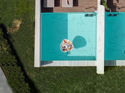 Vogelperspektive eines Pools mit einer Person auf einer Liege und einem Tablett mit Essen im Wasser.