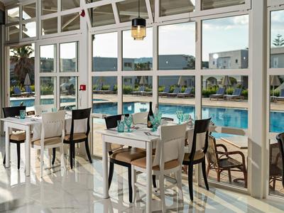 Hell verglaster Wintergarten mit Tischen und Stühlen neben einem blauen Swimmingpool draußen.