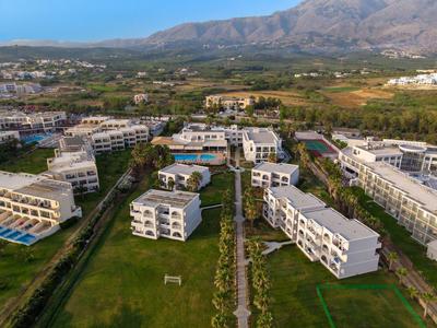 Großes Hotelresort mit mehreren weißen Gebäuden und Grünflächen vor bergiger Landschaft.