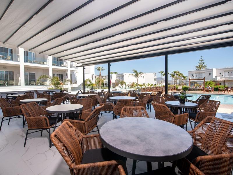 Überdachte Terrasse mit Tischen und Stühlen neben einem Pool in einem Hotel.