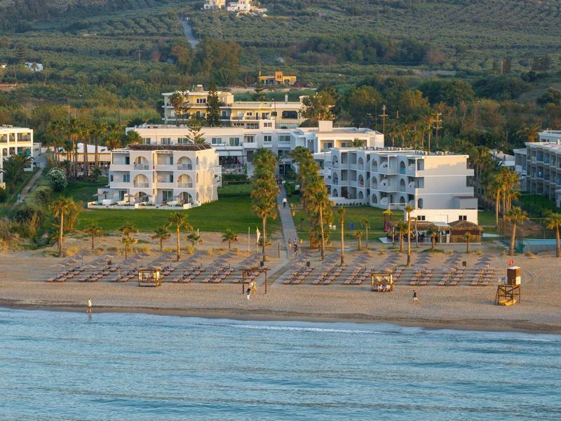 Hotelanlage am Strand mit Liegestühlen und Palmen im Vordergrund