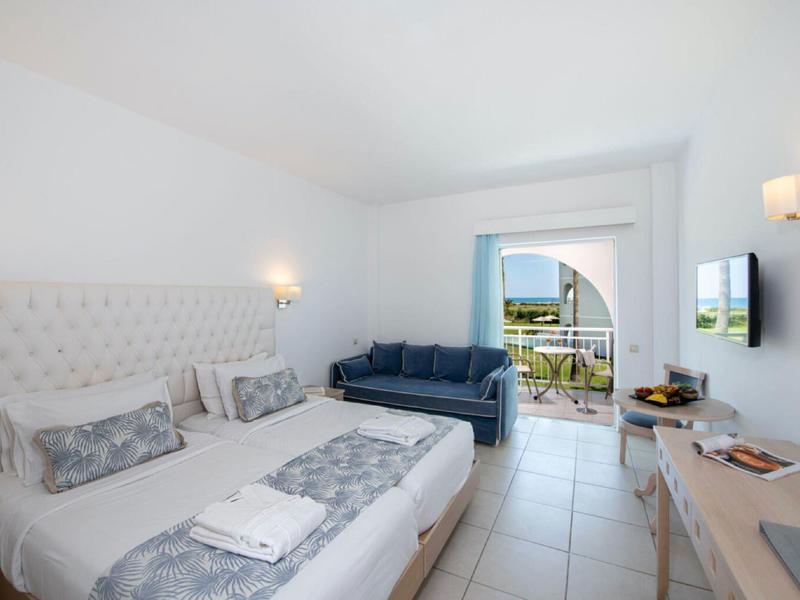 Helles Hotelzimmer mit Doppelbett, Sofa, Flachbildfernseher und Balkon mit Aussicht.