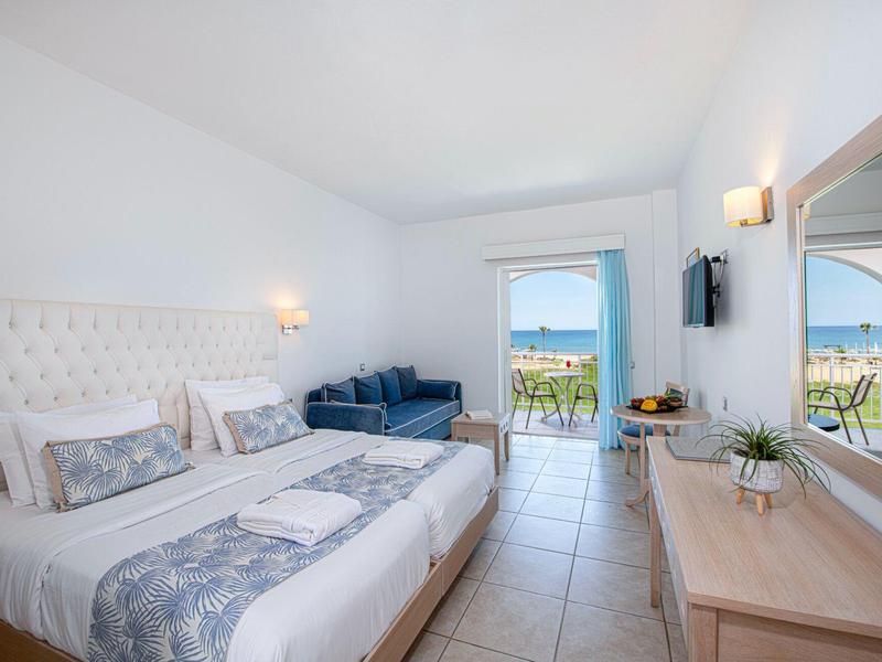 Helles Hotelzimmer mit Doppelbett, Sofa, Schreibtisch und Balkon mit Meerblick.