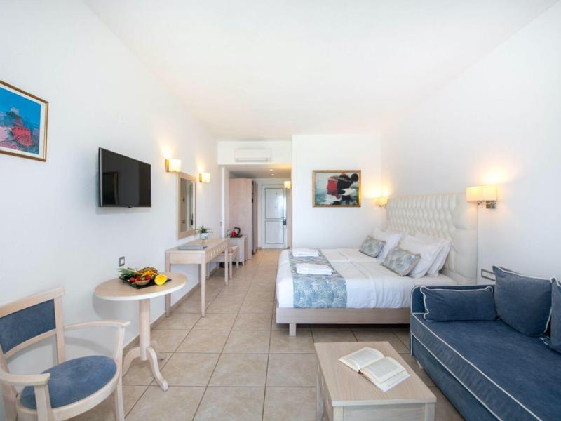 Helles Hotelzimmer mit Bett, Sofa, Stühlen und Wandbild, in modernem, schlichtem Stil.