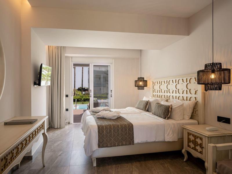 Modern eingerichtetes Hotelzimmer mit Doppelbett, Nachttischen und Zugang zum Balkon mit Meerblick.