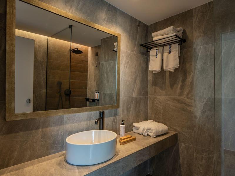 Modernes Badezimmer mit Wandspiegel, Waschbecken, Handtüchern und braunen Fliesen.